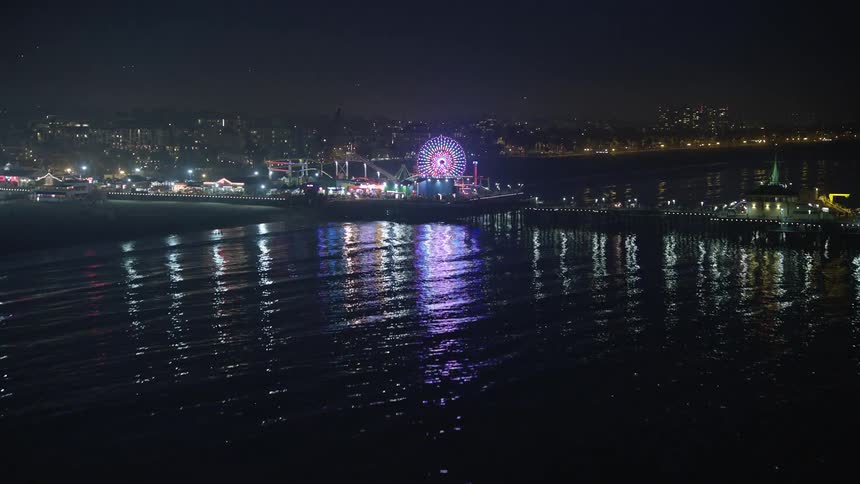 Aerial panorama of a ferris wheel in a beachside park illuminated at night