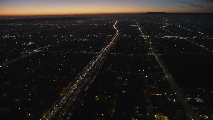A large volume of cars is traveling along a city freeway at night