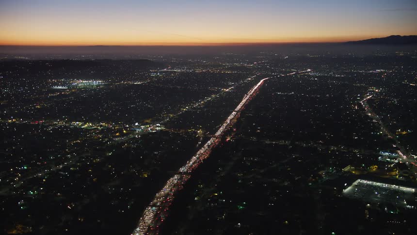 Panorama of a city at dusk with orange sky and vehicle traffic lighting