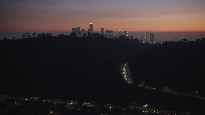 Aerial panorama of a metropolis with skyscrapers surrounded by hills with highways and vehicle traffic at dusk