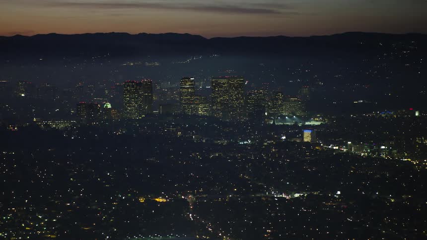 Aerial panorama of a city illuminated at night with the silhouette of mountains around it