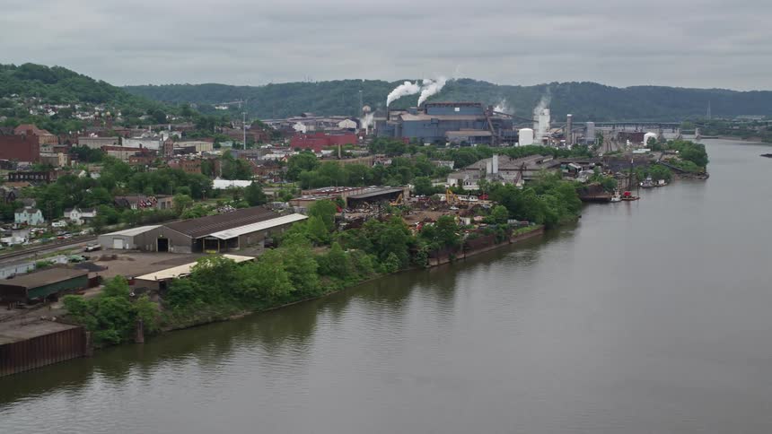 Aerial view of a factory with smoke chimney on the edge of a river in mountains on the horizon