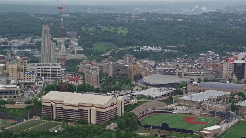 Aerial panorama of an urban city amidst hills and mountains with baseball fields on a blue sky day with clouds
