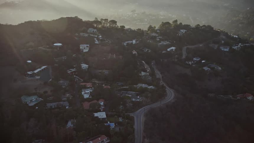 A residential area on a wooded hillside illuminated by the setting sun