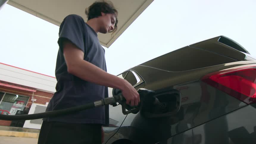 A person refueling a car at a gas station with the fuel nozzle inserted into the cars tank