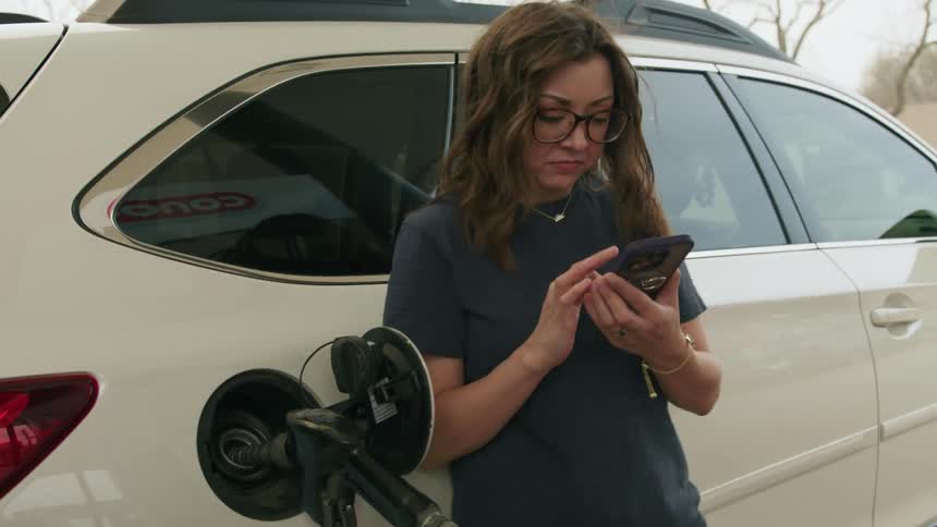A woman looks at her phone as she pumps gas