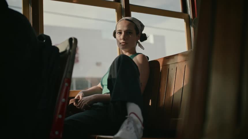 A young woman sitting on urban transportation with wooden seats her leg up and her foot on the seat next to hers
