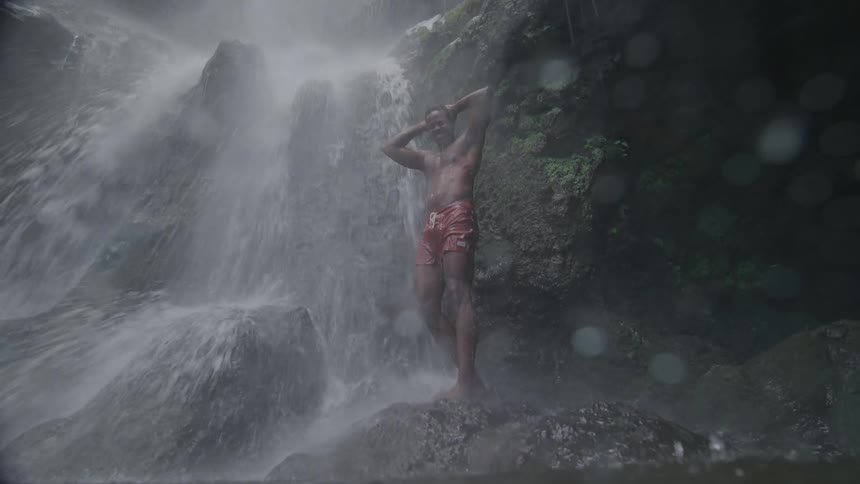 A man stands on rocks beside a water fall
