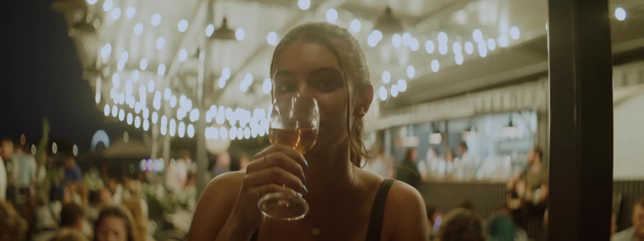 Young woman drinking wine at a crowded venue with hanging lights
