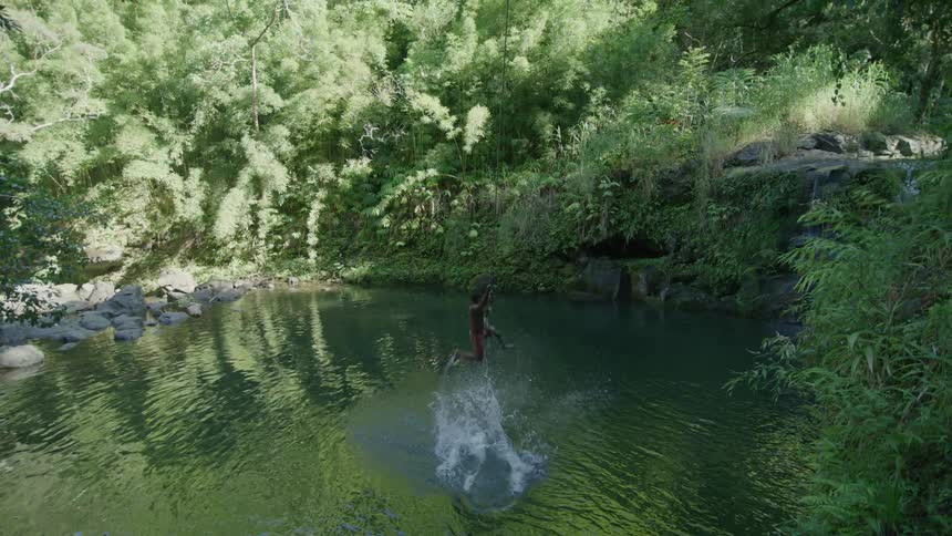 Young man uses a rope swing to drop into the deep pond