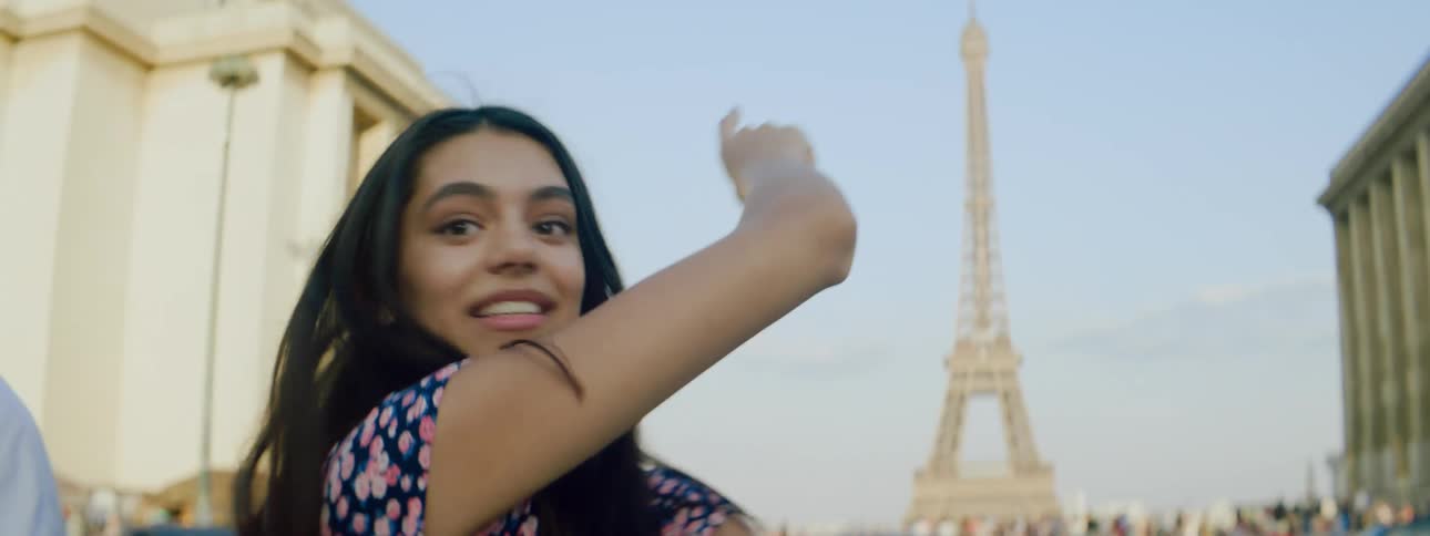Portrait of a happy young woman while standing in a square and pointing at the eiffel tower in paris