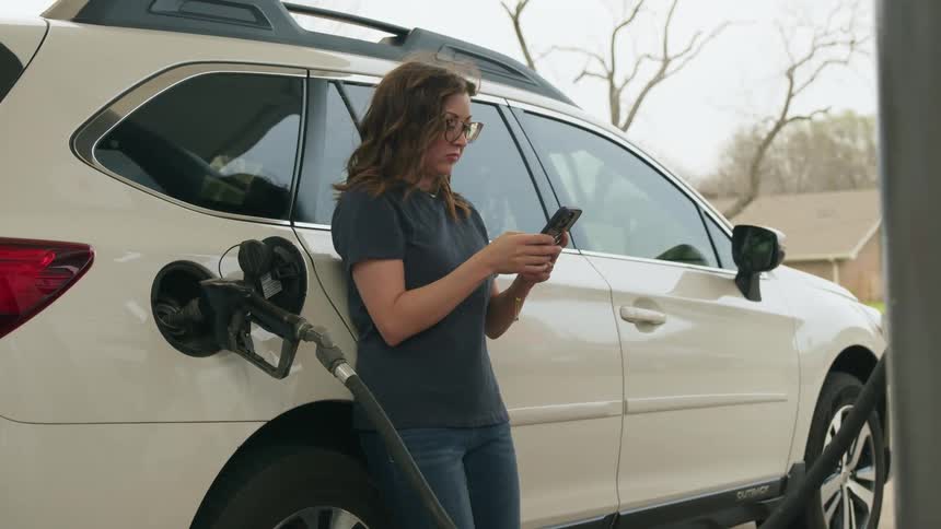 A woman scrolls on a phone while pumping gas
