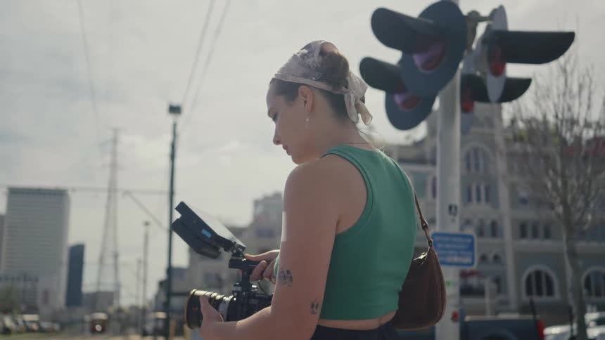 A woman standing is holding a camera and looking at its screen
