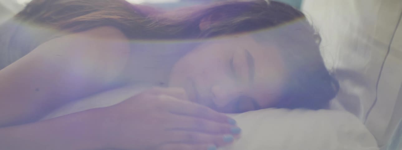A woman sleeps on her stomach on a white pillow in bed