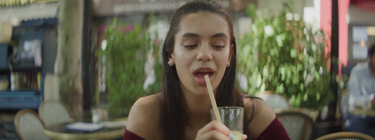 Portrait of a young woman sitting drinking a juice through a straw outside a restaurant