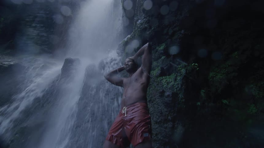 A man stands next to a waterfall rinsing his hair