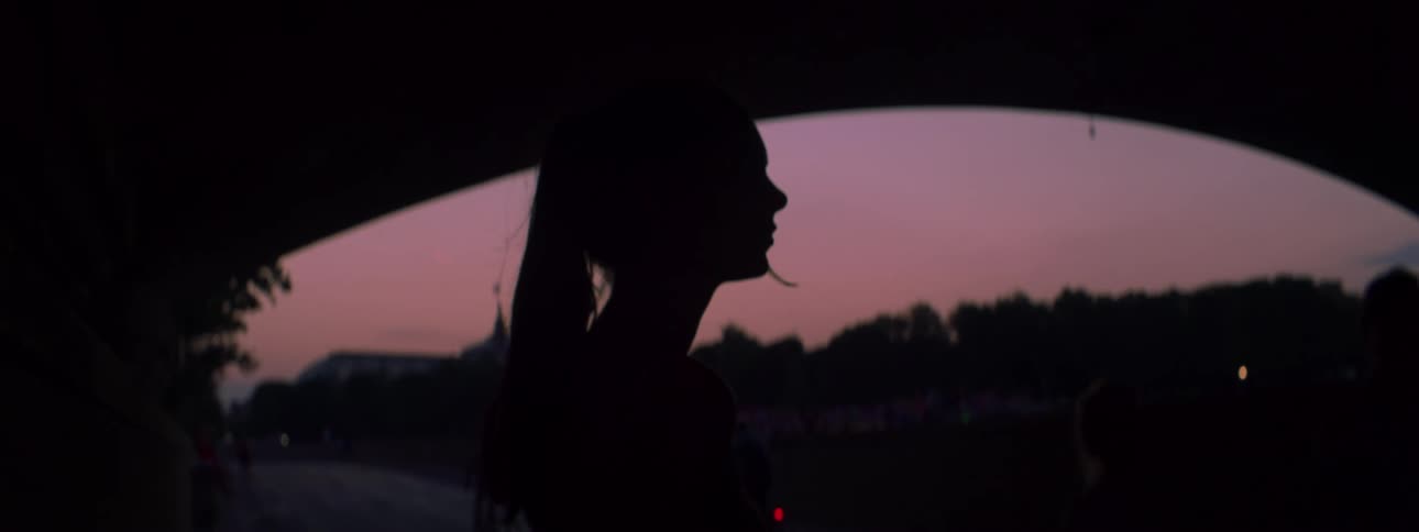 A side silhouette of a young woman outdoors with the purple sky