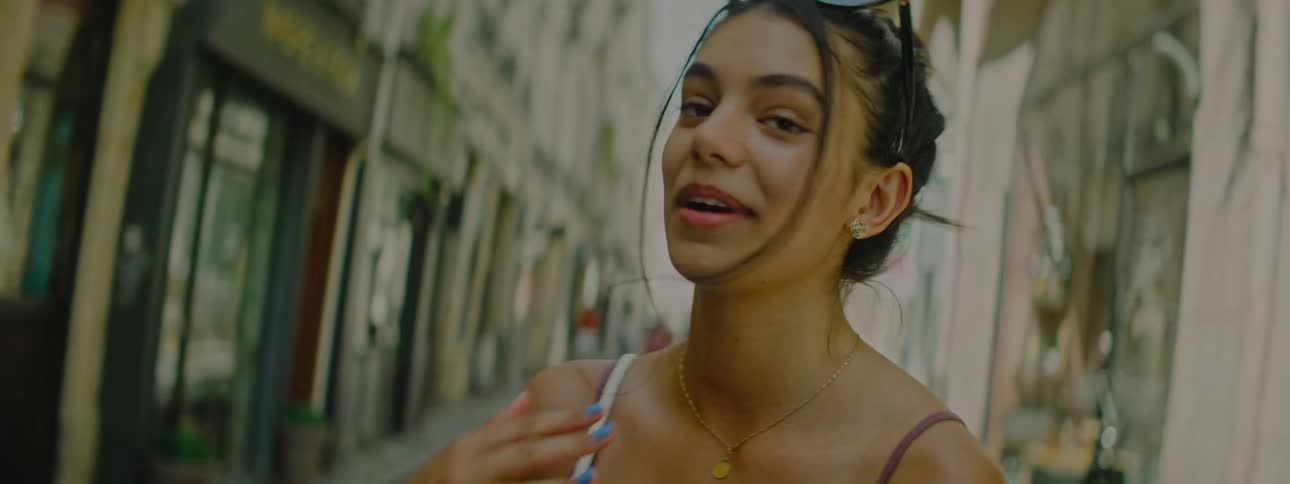 Portrait of a young woman smiling and talking while walking in an alley with commercial stores in the city