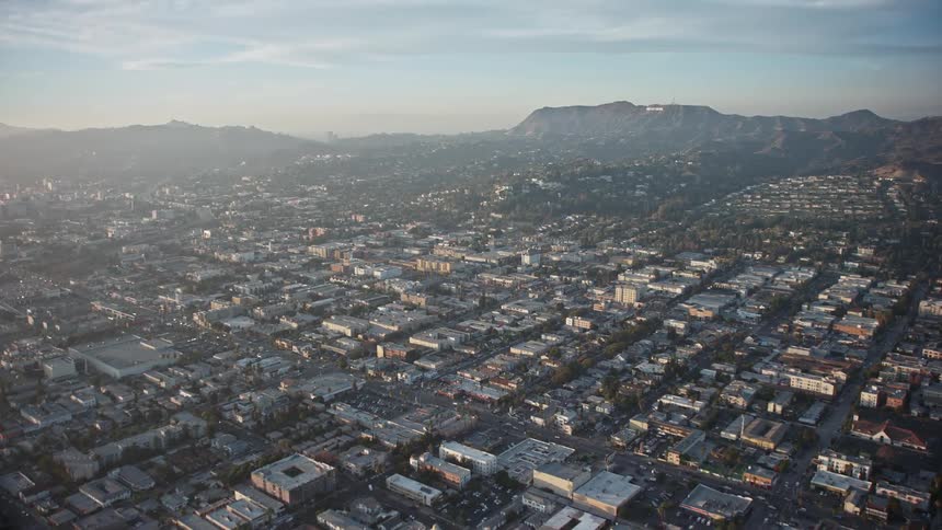 A cityscape is illuminated by the soft light of sunrise with mountains in the background