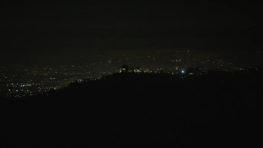 Aerial view of city lights over a hill at night