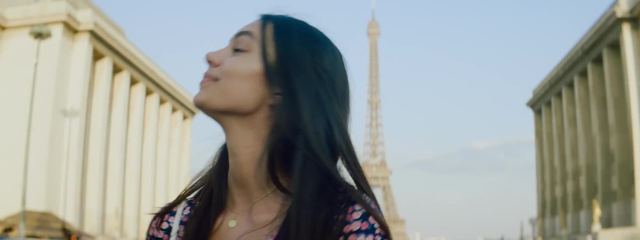 Portrait of a young smiling woman pointing back towards the eiffel tower in france