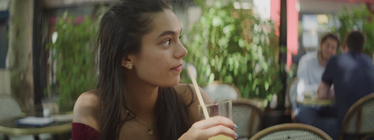 Portrait of a young woman sitting on benches in a restaurant and drinking a juice