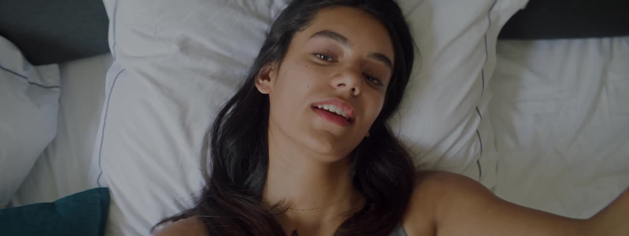 A young woman lying in bed filming herself talking