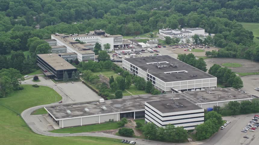 Aerial view of a large building complex surrounded by greenery and a parking lot