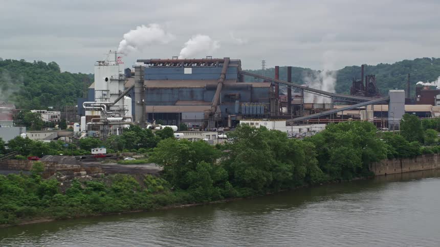 Aerial view of an industrial facility by a river with smoke emissions