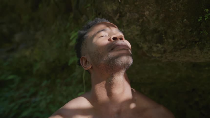Portrait of a man closing and opening his eyes while shirtless in a natural environment with a sun reflection