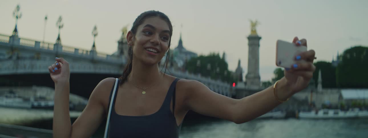A young woman traveling in Paris takes a selfie video in front of a bridge