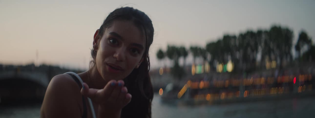 A young woman in front of a river smiles sends kisses and makes funny faces