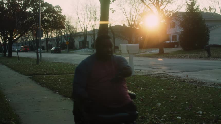 Man rides his wheelchair down the sidewalk as the sunrises in the suburban neighborhood