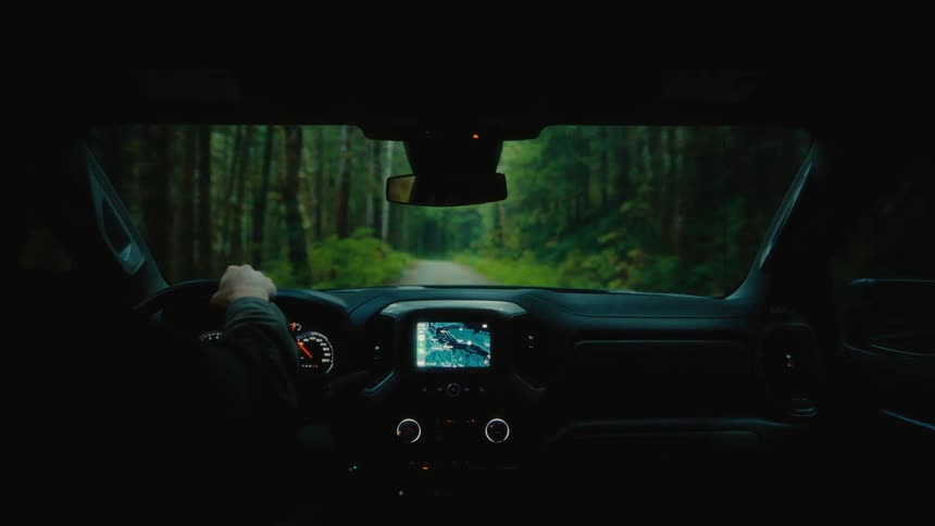 Inside view of the dashboard and windshield of a vehicle with a person driving on a narrow road through the forest