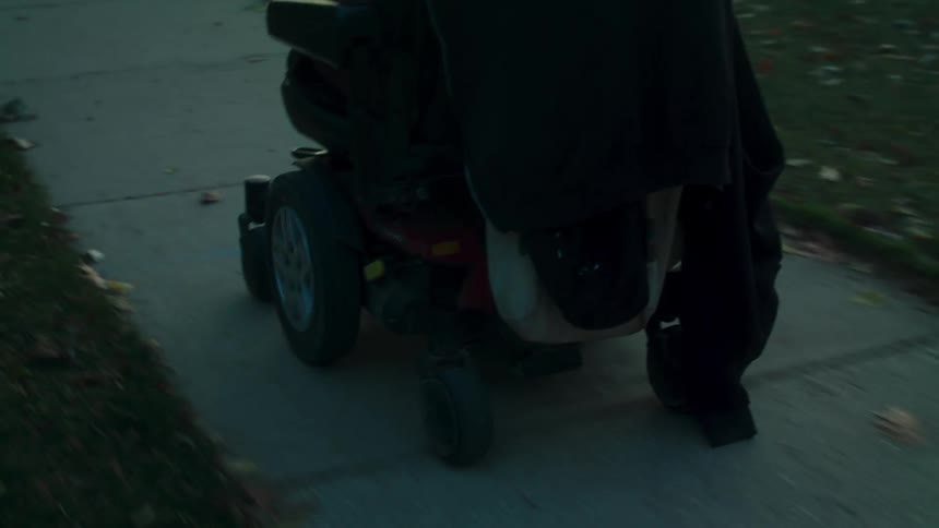 A black man in a wheelchair moving down a sidewalk