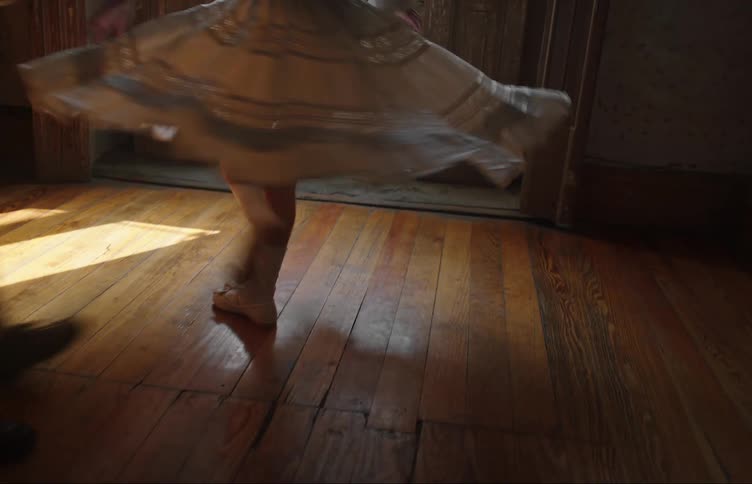 Two children dancing in an old room with wooden floor and a door