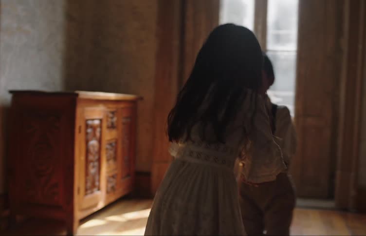 Two children hold hands and spin around laughing and dancing in an old house