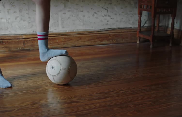 A child with socks is playing with a soccer ball with a smaller child in a room