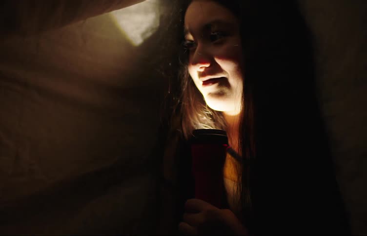 Two children playing with a flashlight under bedsheets at night