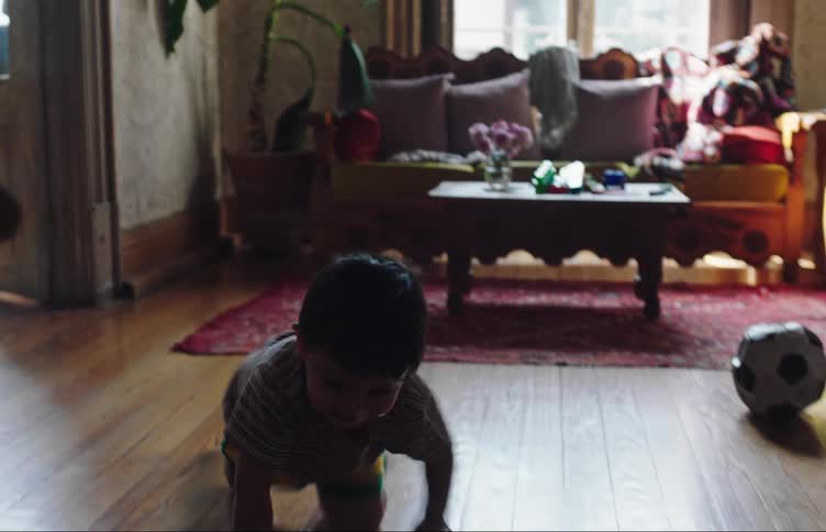 A young boy excitedly crawls on the hardwood floor inside of a home