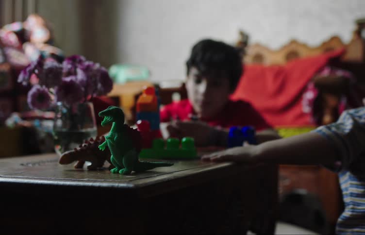 A boy is playing with a dinosaur toy and there is another older boy behind him