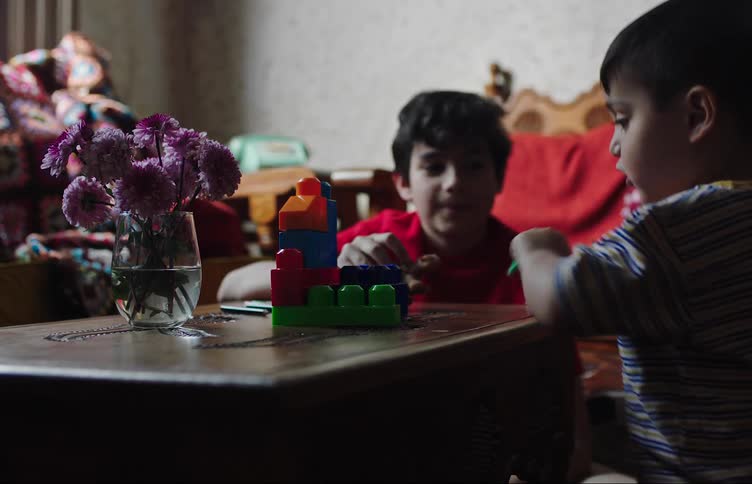 A child and a toddler play with blocks and action figures at a small table
