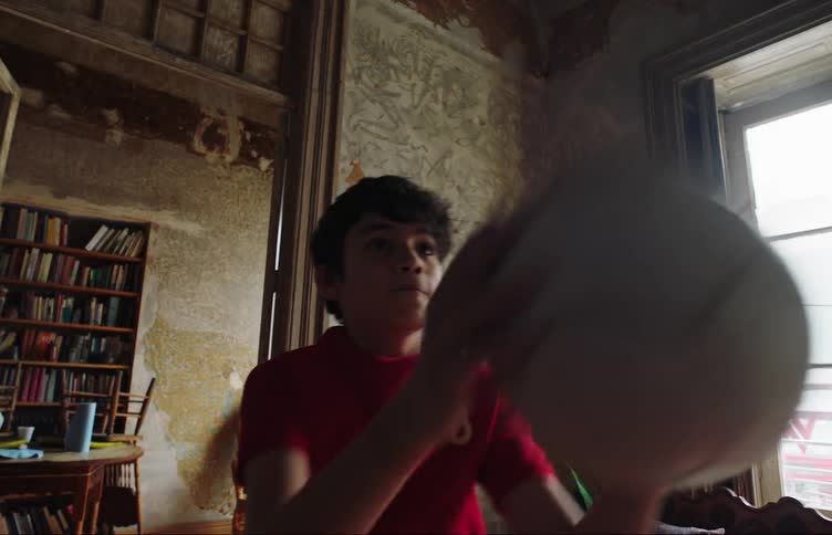 A boy repeatedly throws a soccer ball against the wall of his room
