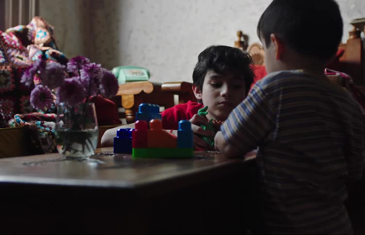 Two boys at a table playing with toy dinosaurs and blocks