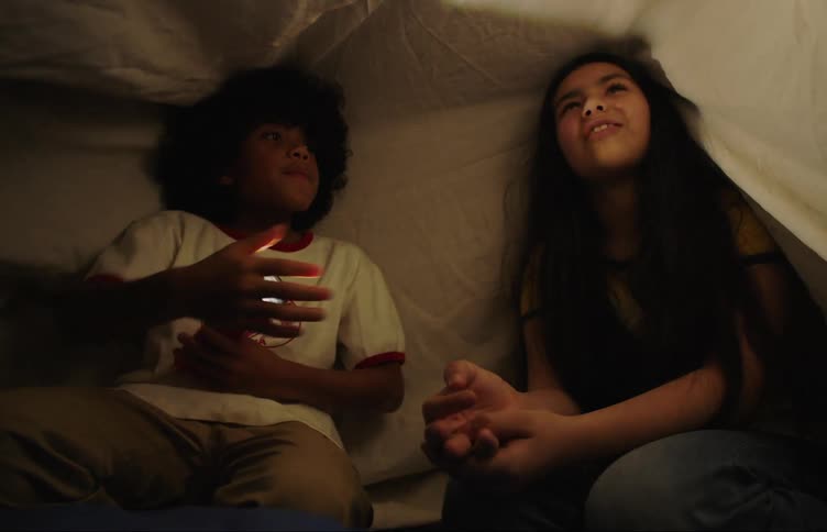 Two children play with a flashlight under the covers