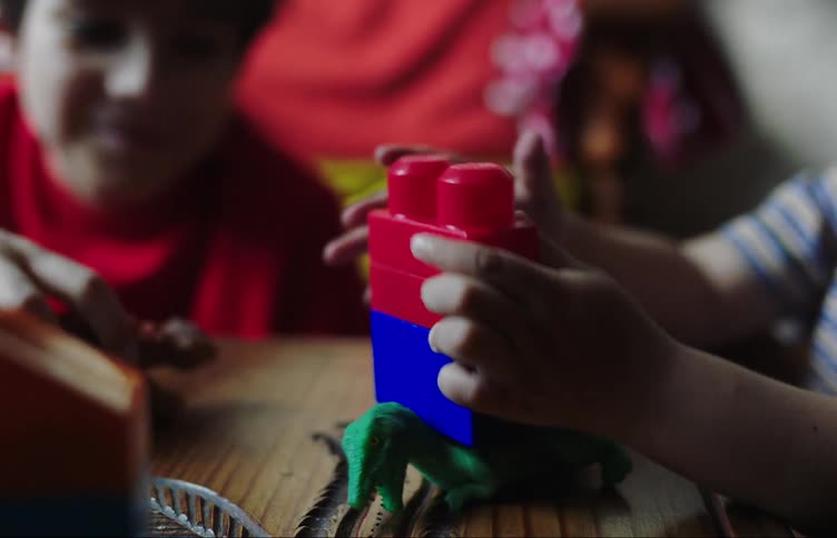 Two little boys are playing with toys on a table and there are some rubber dinosaurs