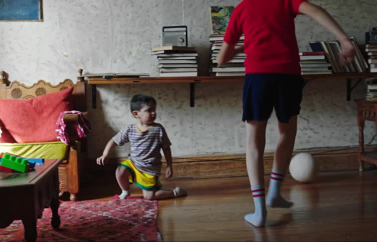 Two children kick a soccer ball around the living room