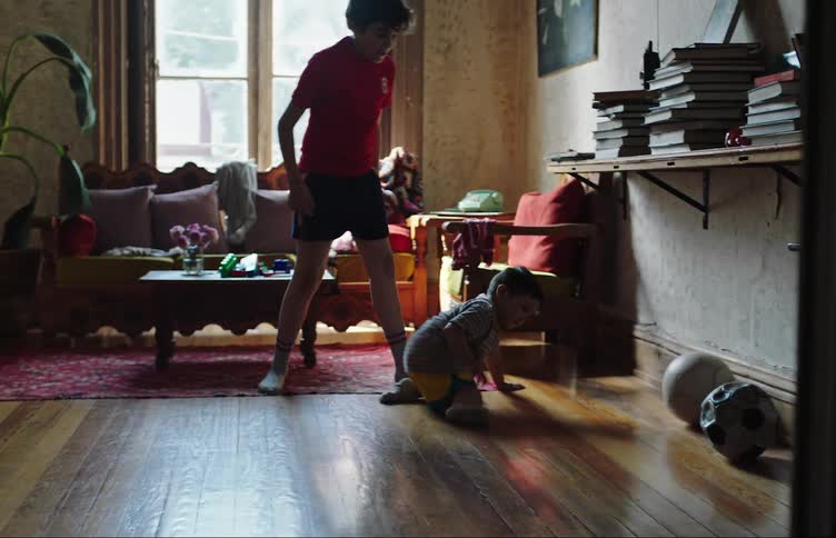 Two children playing soccer in a cluttered room