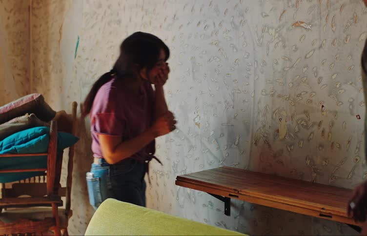 Man and woman stumble while carrying furniture and smile while examining damage to the wall