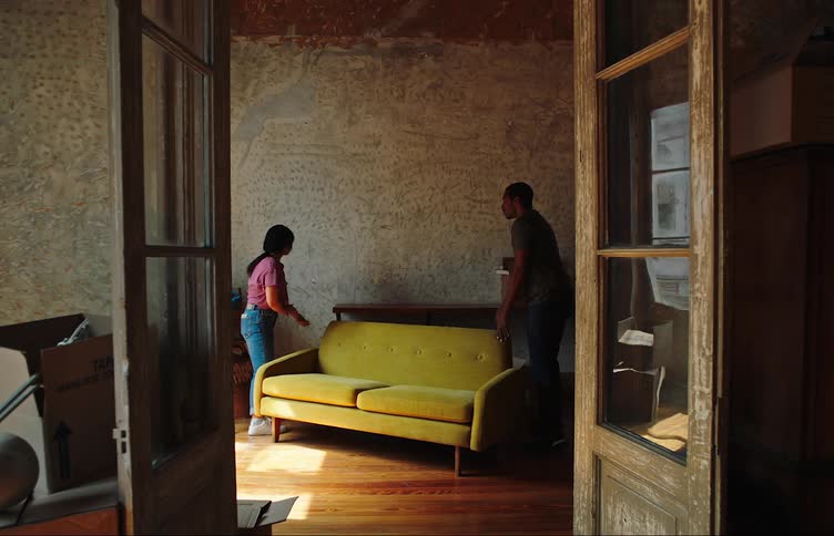 Two people carry a couch into the living room